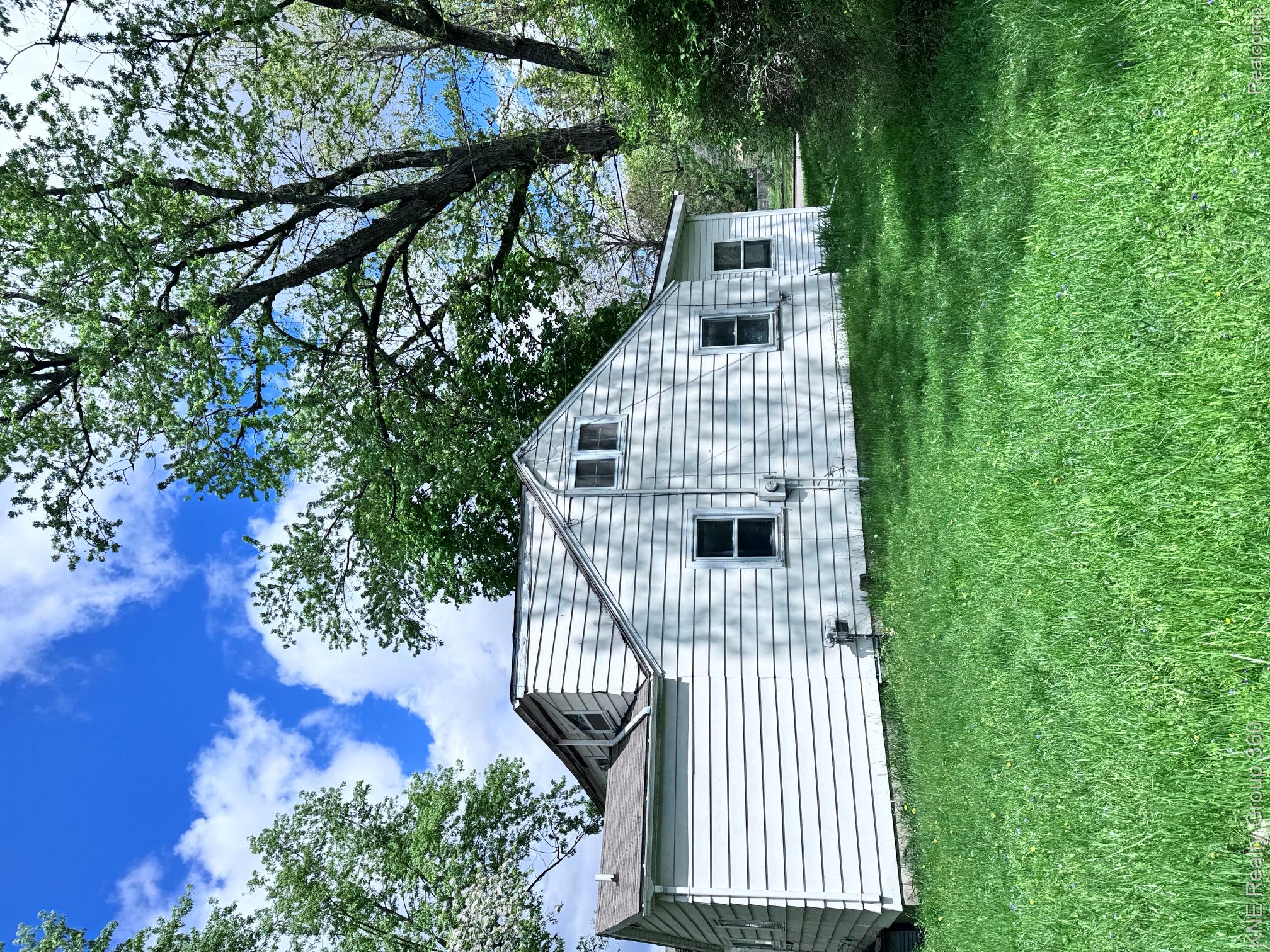 4928 Hughes Road Lansing, MI 48910 - Photo 31 of 35 White siding exterior with multiple windows, a sloped roofline, and established trees providing natural shade