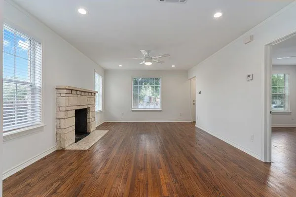 an empty room with wooden floor fireplace and windows