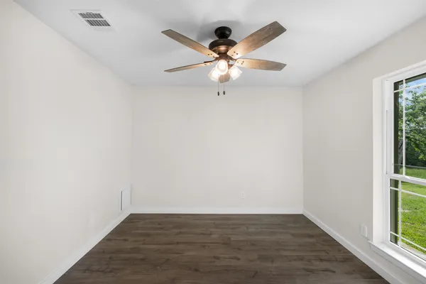 an empty room with wooden floor fan and windows