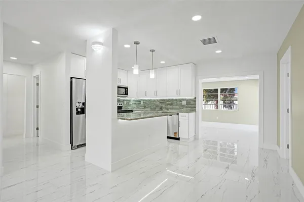 a view of kitchen with stainless steel appliances kitchen island granite countertop a refrigerator and white cabinets