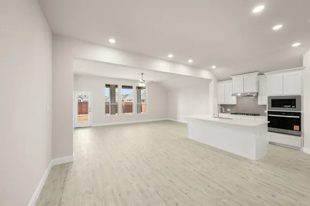 a large white kitchen with stainless steel appliances granite countertop a stove a sink a refrigerator white cabinets and wooden floor