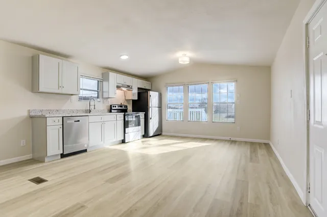 a kitchen with stainless steel appliances granite countertop a stove top oven a sink dishwasher and a refrigerator with wooden floor