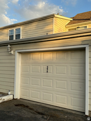 254 Meadow Lane Centerville, UT 84014 - Photo 34 of 34 Attached garage with panel door, exterior wall lantern, house numbers, and light-colored siding