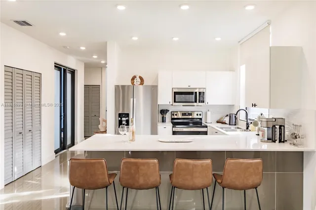 a kitchen with stainless steel appliances a dining table chairs refrigerator and sink