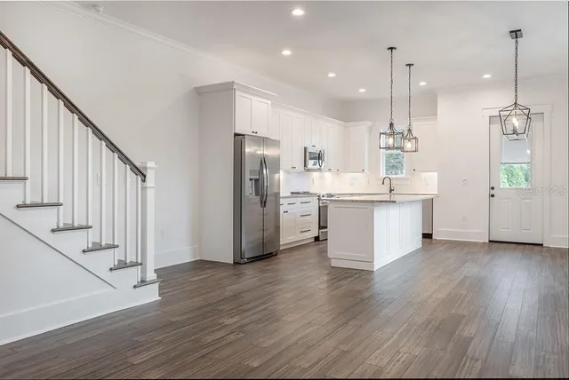 a kitchen with stainless steel appliances kitchen island wooden floors cabinets and a chandelier