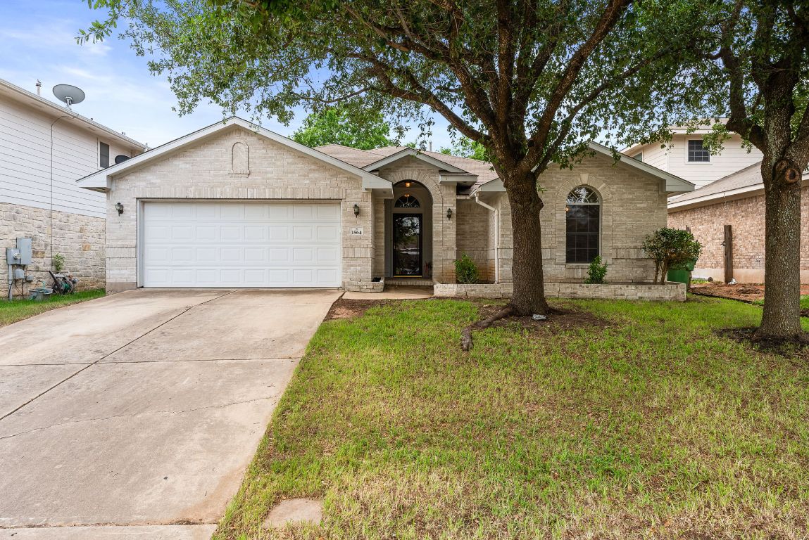 Single story home featuring a front yard, concrete driveway, an attached garage, and brick siding