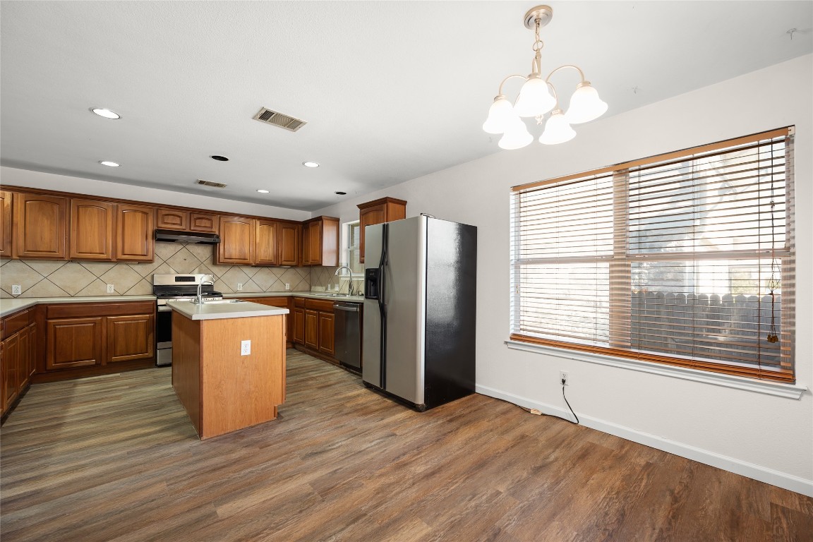 1564 Lorson Loop Round Rock, TX 78665 - Photo 8 of 27 Kitchen featuring brown cabinetry, pendant lighting, appliances with stainless steel finishes, a center island with sink, and decorative backsplash