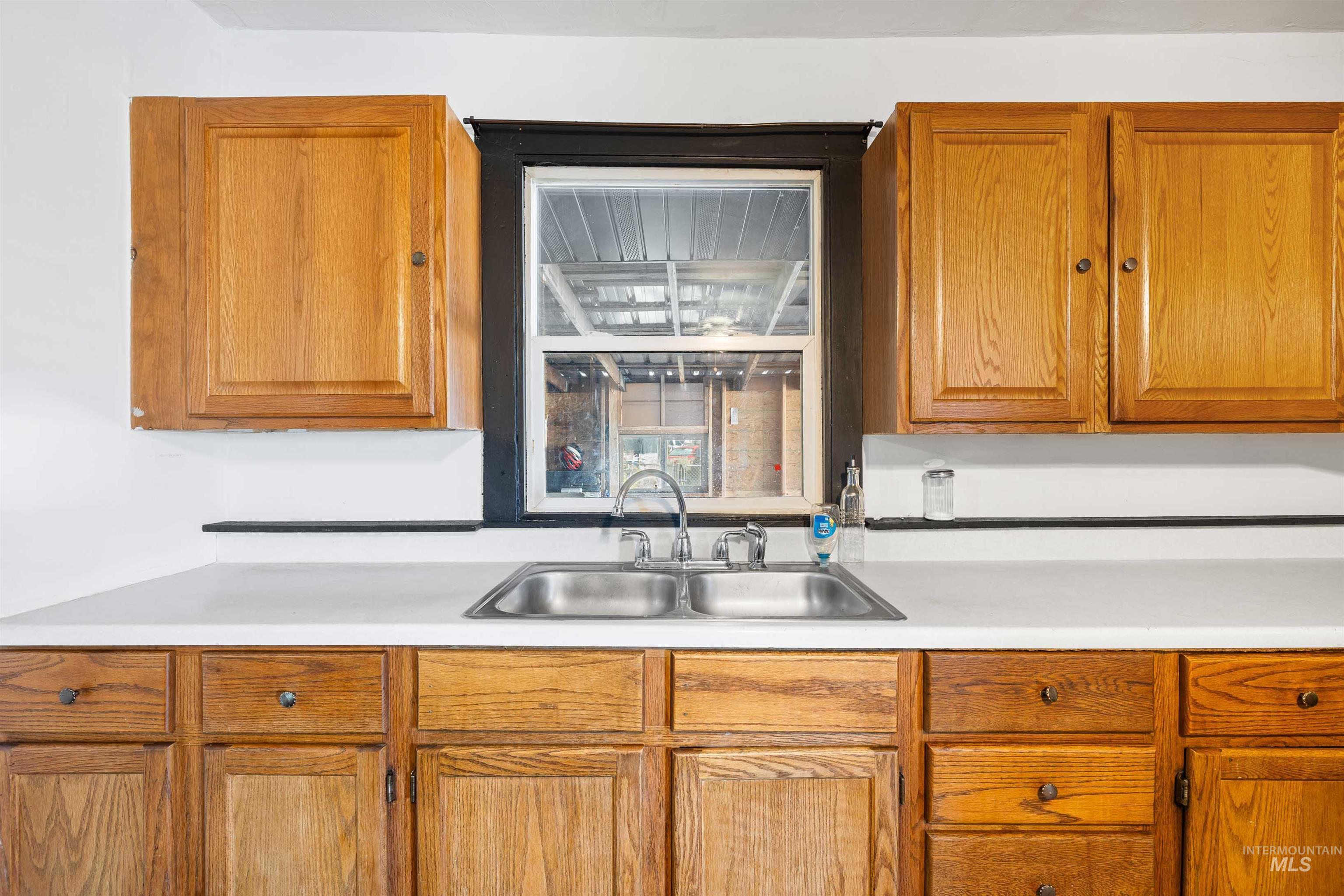 102 East 6th Street Rupert, ID 83350 - Photo 9 of 27 Kitchen features wood-finish cabinetry, a double-basin stainless steel sink with a chrome faucet, and white countertops