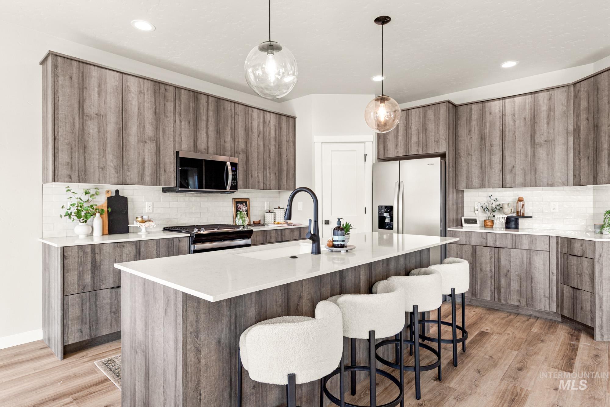 5487 West Yarnell Street Eagle, ID 83616 - Photo 14 of 30 Kitchen with hanging light fixtures, modern cabinets, light stone counters, stainless steel appliances, and a kitchen island with sink