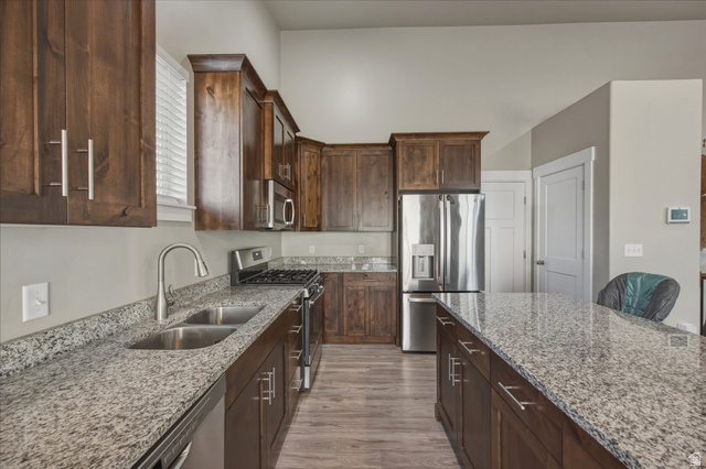 45 Memory Lane Tooele, UT 84074 - Photo 11 of 30 Kitchen with stainless steel appliances, dark wood finish cabinets, light stone counters, and light wood-style flooring