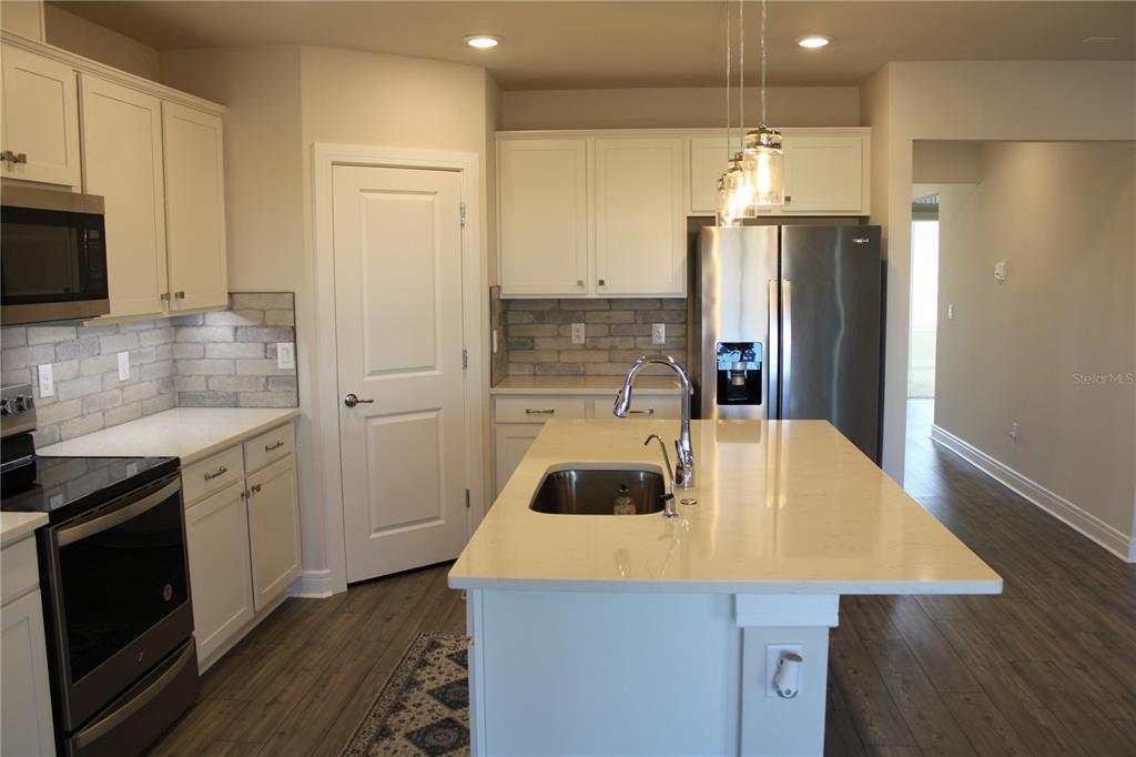 8232 Reefbay Cove Parrish, FL 34221 - Photo 7 of 64 a kitchen that has a refrigerator a stove a sink and white cabinets with wooden floor