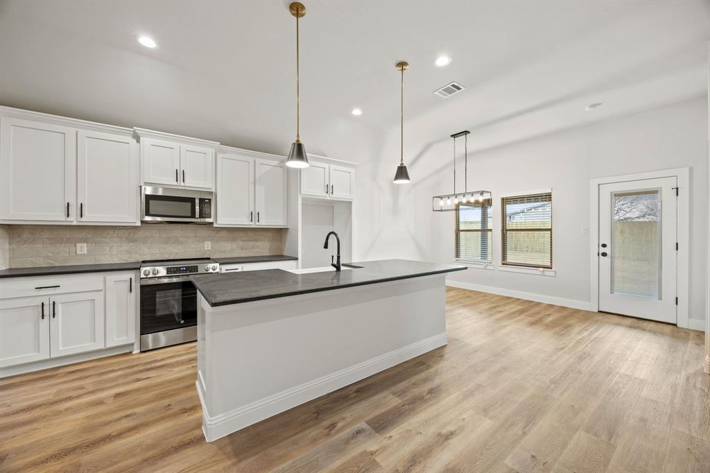 104 Maverick Trail Valley View, TX 76272 - Photo 11 of 30 a large kitchen with stainless steel appliances granite countertop a stove a sink and a wooden floor