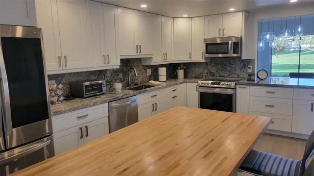 a kitchen with stainless steel appliances granite countertop a stove top oven a sink a refrigerator and white cabinets