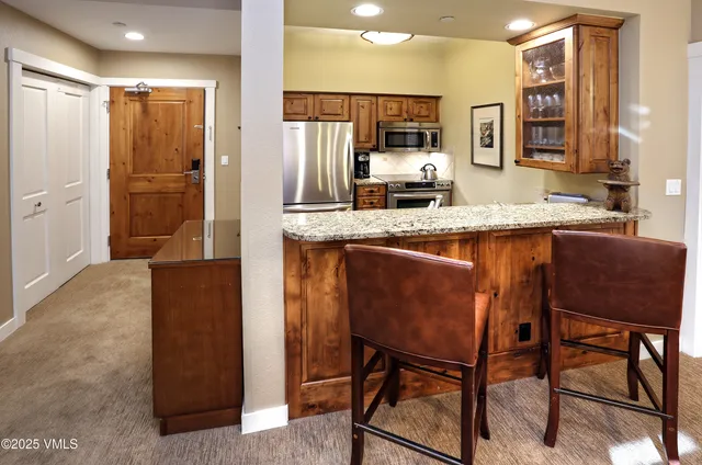 a kitchen with stainless steel appliances granite countertop a table chairs refrigerator and sink