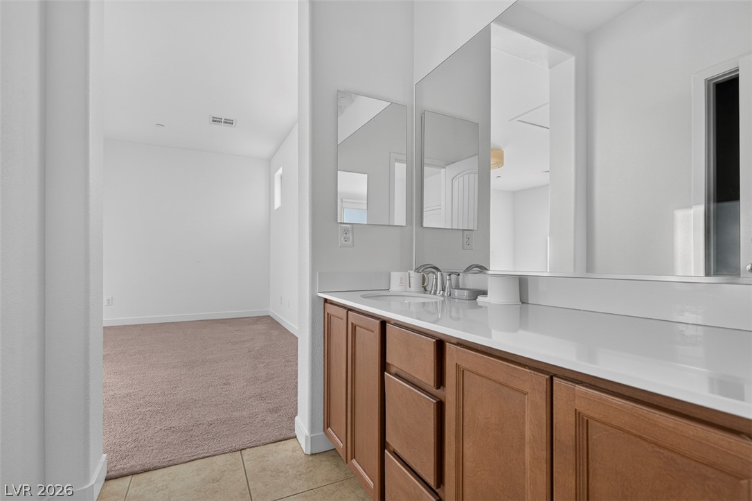 1100 East Sunset Road Henderson, NV 89011 - Photo 40 of 58 A streamlined vanity with dual mirrors complements the neutral-toned flooring, leading to a spacious, carpeted room.