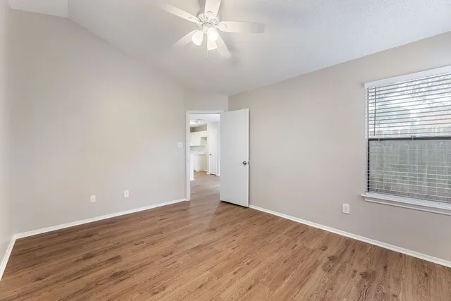 an empty room with wooden floor chandelier fan and windows