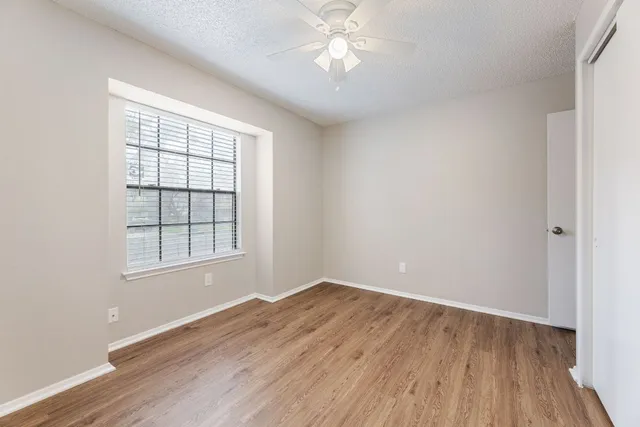 an empty room with wooden floor chandelier fan and windows