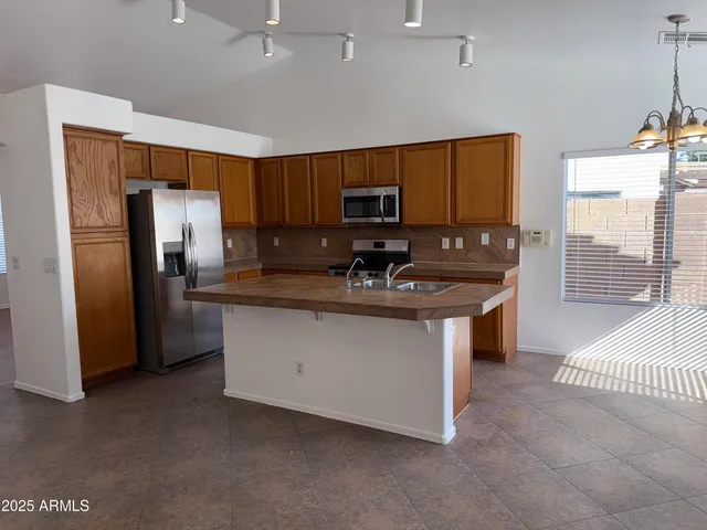 a kitchen with stainless steel appliances granite countertop a stove a sink a refrigerator a window and a kitchen island