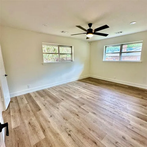 an empty room with wooden floor fan and windows