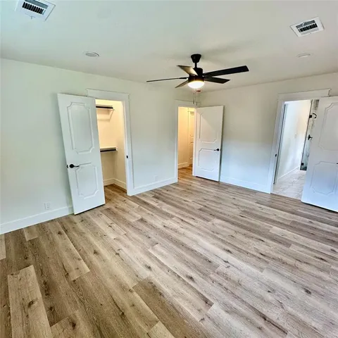 an empty room with wooden floor ceiling fan and windows