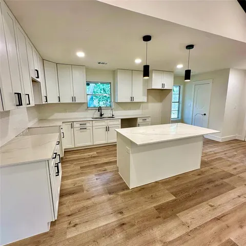 a large white kitchen with kitchen island a stove a sink dishwasher and white cabinets with wooden floor
