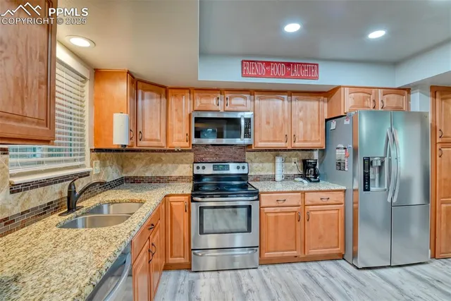 a kitchen with stainless steel appliances granite countertop a stove top oven a refrigerator and a sink with wooden floor
