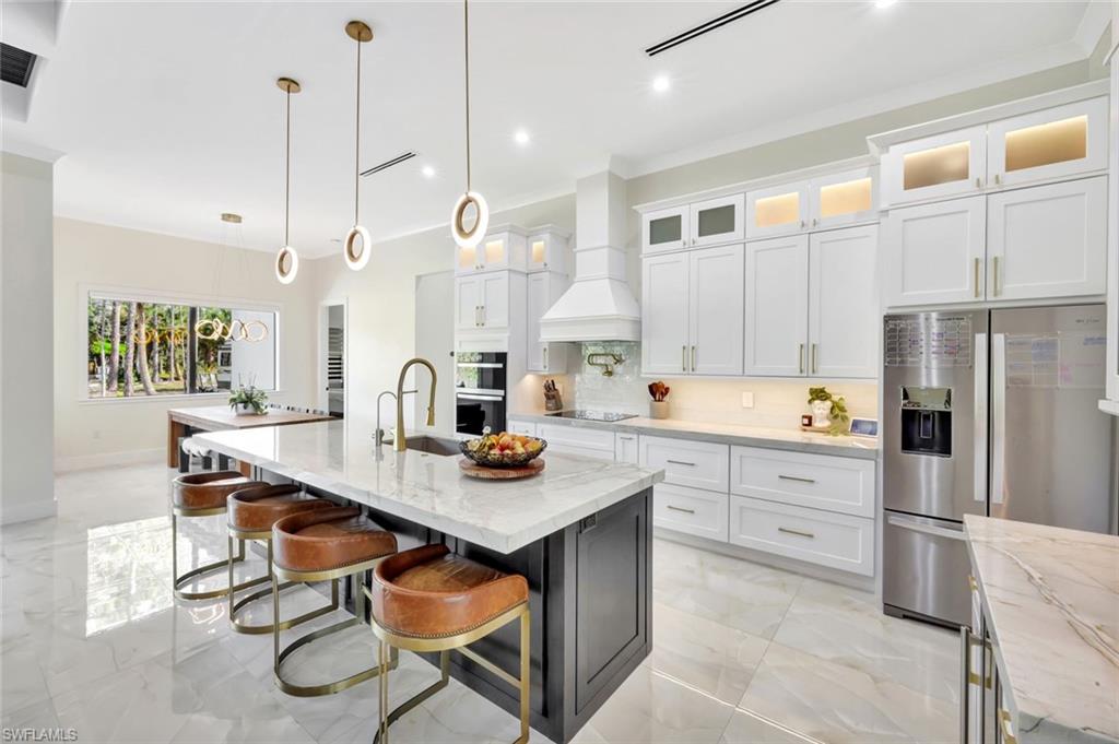 2546 4th Street Northwest Naples, FL 34120 - Photo 2 of 44 Kitchen featuring stainless steel fridge, white cabinetry, light stone counters, glass insert cabinets, and a breakfast bar area