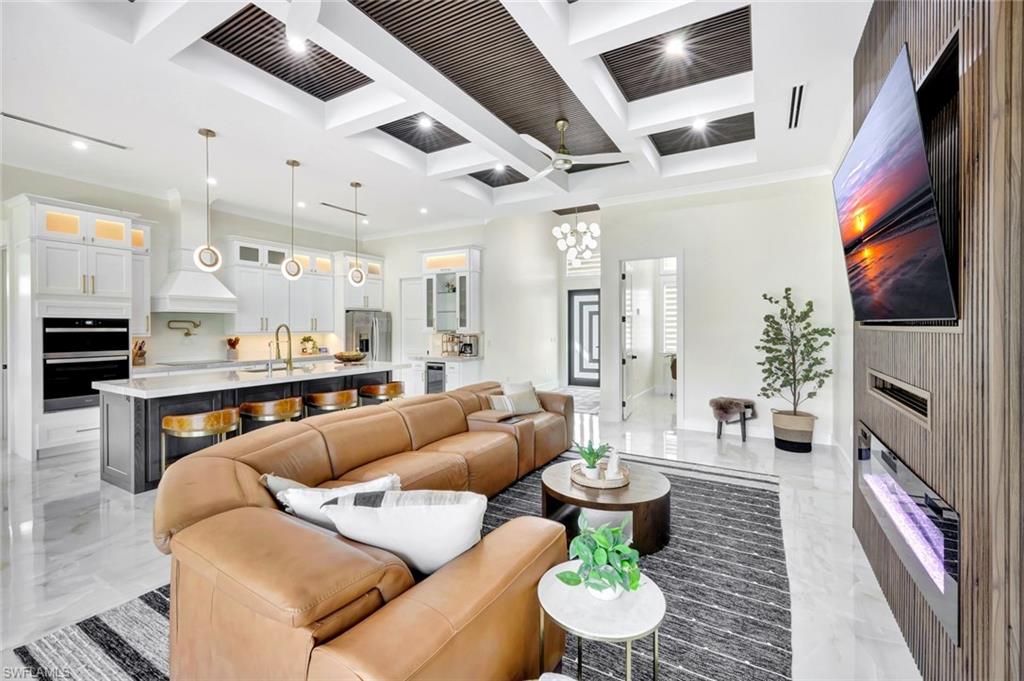 2546 4th Street Northwest Naples, FL 34120 - Photo 5 of 44 Living area with a fireplace, coffered ceiling, light marble finish flooring, a ceiling fan, and a chandelier