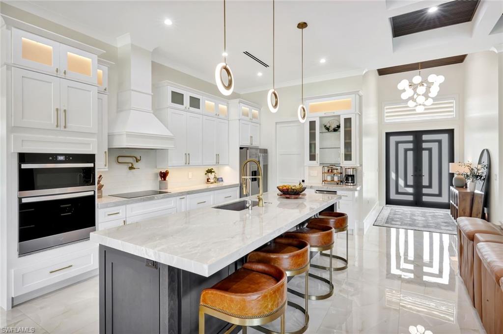 2546 4th Street Northwest Naples, FL 34120 - Photo 8 of 44 Kitchen with glass insert cabinets, a kitchen bar, white cabinets, light stone counters, and ornamental molding