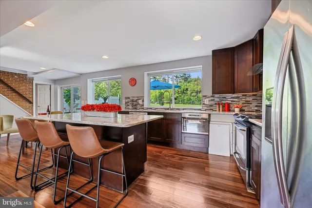 a kitchen with stainless steel appliances granite countertop a refrigerator a stove a sink dishwasher and a dining table with wooden floor