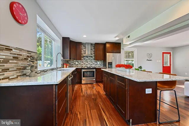 a kitchen with kitchen island granite countertop wooden cabinets a sink dishwasher and a stove with wooden floor