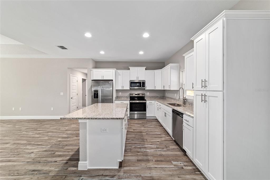 13359 Southwest 80th Street Dunnellon, FL 34432 - Photo 25 of 64 a large kitchen with kitchen island a stove a sink a refrigerator and white cabinets with wooden floor