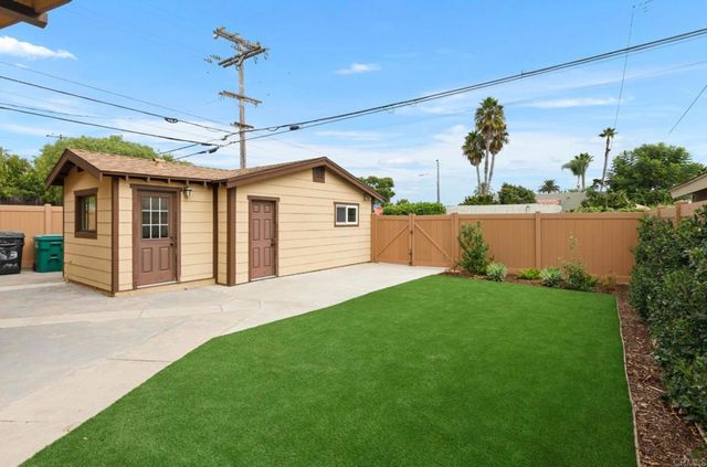 a view of a yard in front of a house with plants and wooden fence