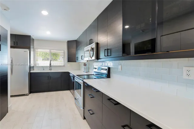 a large kitchen with stainless steel appliances a sink dishwasher a refrigerator and a stove with wooden floor