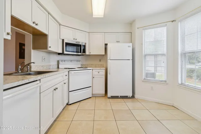 a kitchen with white cabinets a sink a stove a refrigerator and a window