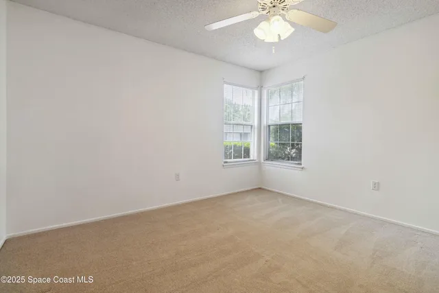 an empty room with windows and chandelier fan