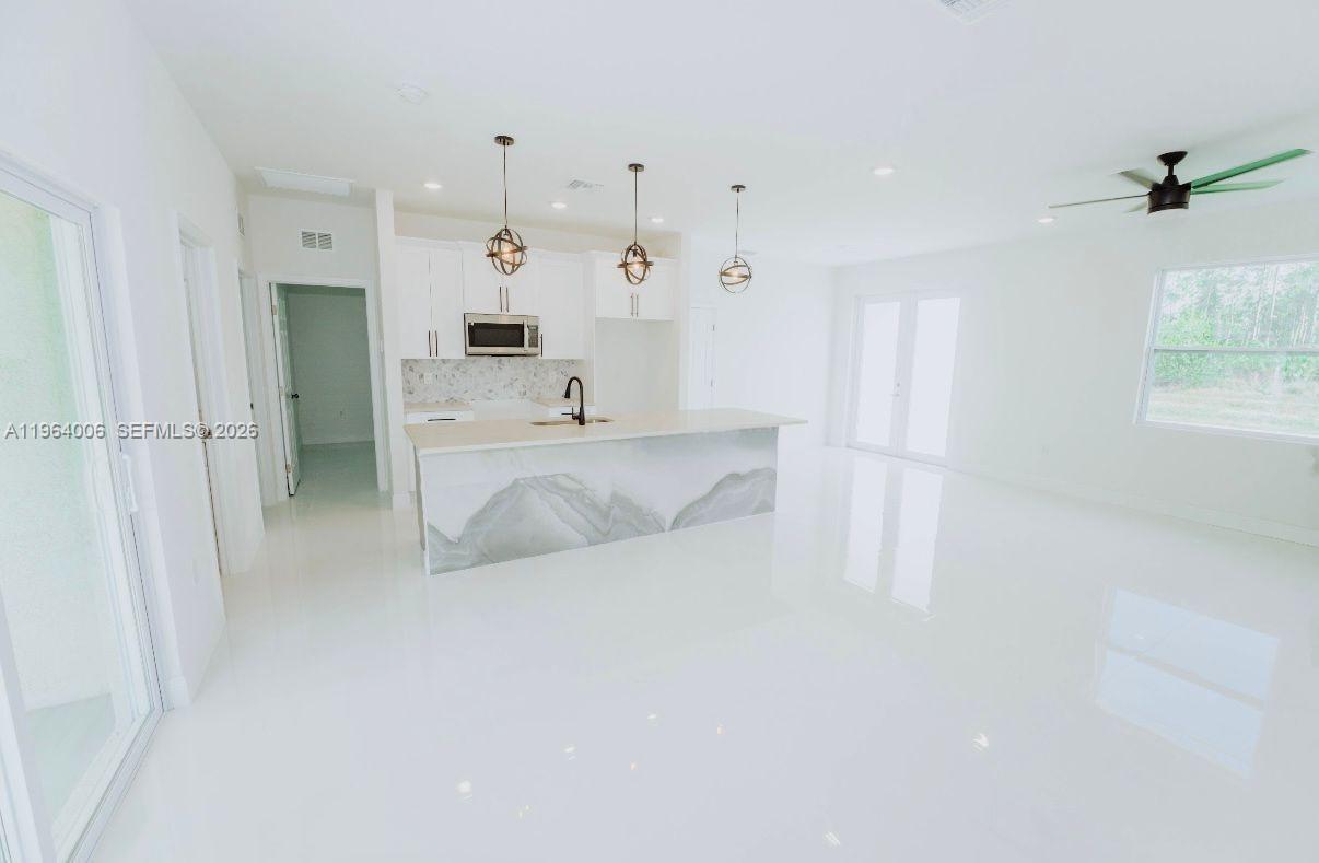 4405 East 7th Street Lehigh Acres, FL 33972 - Photo 5 of 6 a large white kitchen with kitchen island a sink a stove and a refrigerator
