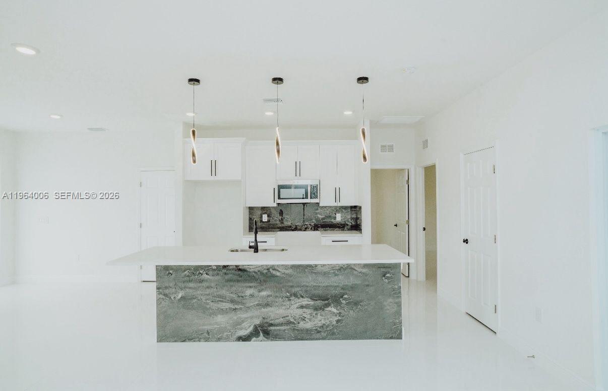 4405 East 7th Street Lehigh Acres, FL 33972 - Photo 6 of 6 a large white kitchen with kitchen island granite countertop a large counter top and a sink