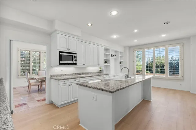 a large kitchen with stainless steel appliances granite countertop a stove a sink a refrigerator and white cabinets with wooden floor