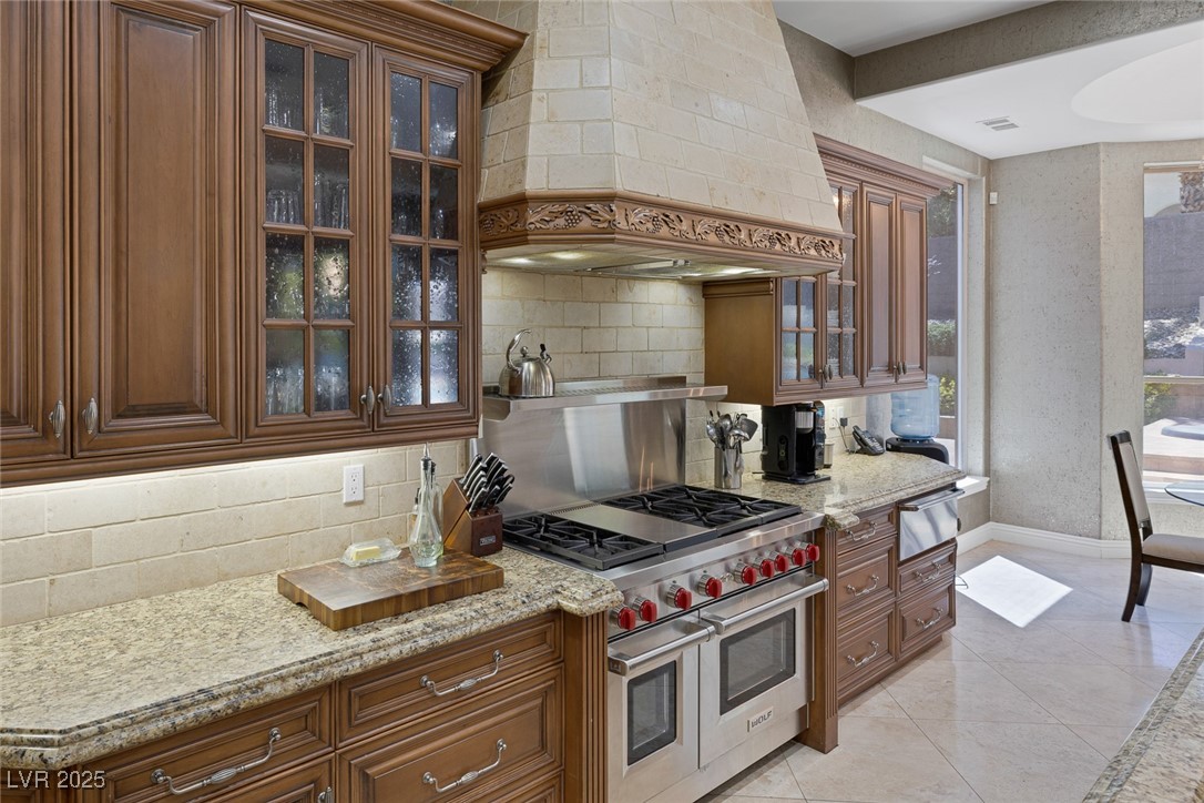 1545 Villa Rica Drive Henderson, NV 89052 - Photo 21 of 61 Kitchen with decorative backsplash, custom exhaust hood, range with two ovens, light stone counters, and brown cabinetry