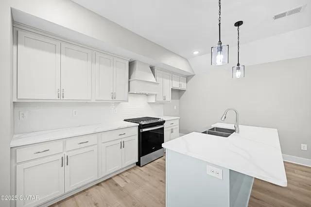 a kitchen with a sink dishwasher and white cabinets with wooden floor