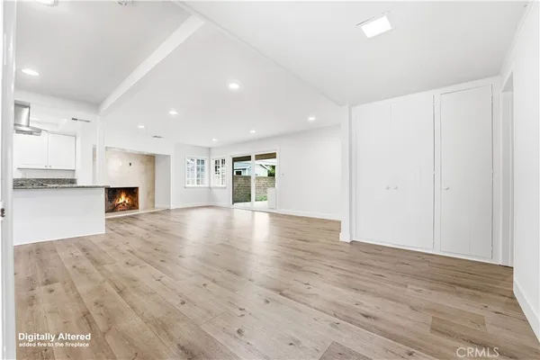 an empty room with wooden floor kitchen fireplace and windows