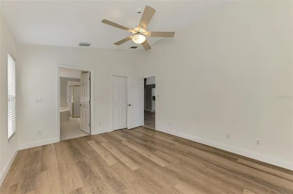 an empty room with wooden floor ceiling fan and windows