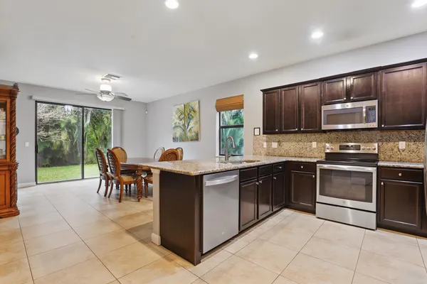 a kitchen with stainless steel appliances granite countertop a stove top oven a sink dishwasher a dining table and chairs with wooden floor