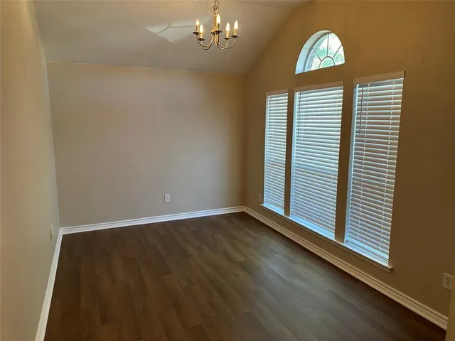 an empty room with wooden floor chandelier and windows