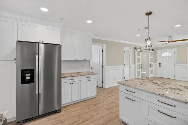 a kitchen with granite countertop a refrigerator a sink and white cabinets