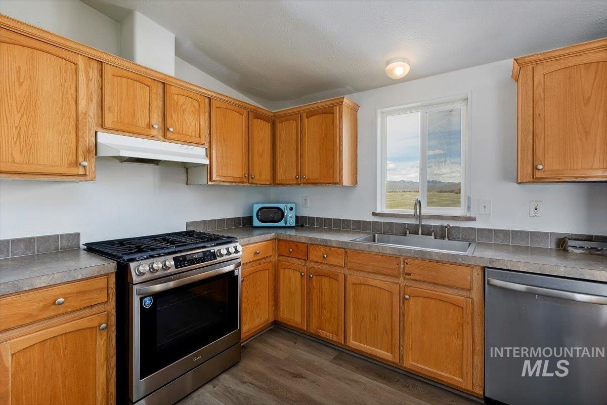 501 Timber Avenue Fairfield, ID 83327 - Photo 10 of 27 Kitchen featuring stainless steel appliances, dark wood finished floors, vaulted ceiling, wood finish cabinetry, and light countertops