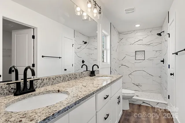 a bathroom with a granite countertop double vanity sink toilet and shower