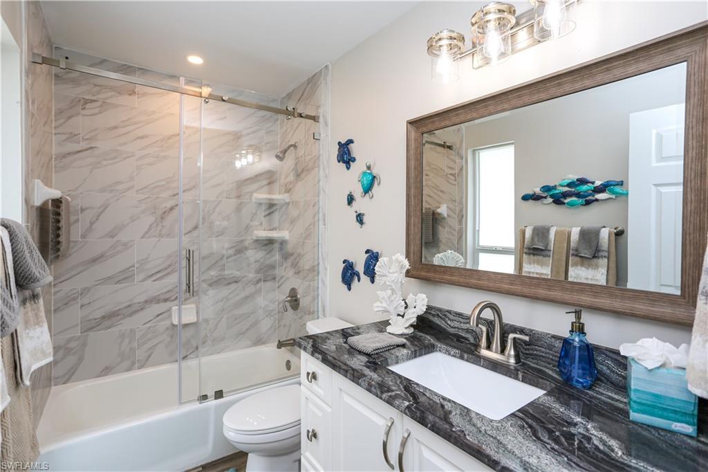 195 Peppermint Lane, Unit 884 Naples, FL 34112 - Photo 22 of 50 a bathroom with a granite countertop sink toilet a mirror a bathtub and shower