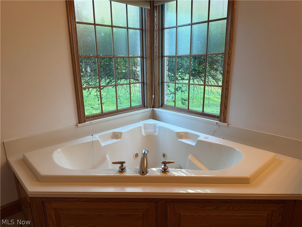 2363 Tabor Ridge Road Northeast New Philadelphia, OH 44663 - Photo 27 of 42 Corner jetted tub set within a wood-finish cabinet surround, featuring dual window panels with natural wood trim